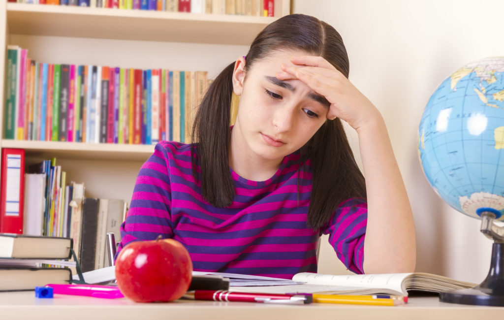 40278343 - schoolgirl overwhelmed by her studies, sitting in a table full of notebooks and pencils and pens